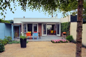 A modern house with a covered patio, a barbecue grill, and colorful outdoor furniture.