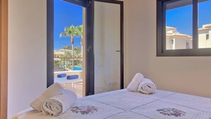 Une chambre d’hôtel avec un lit, deux serviettes enroulées, une fenêtre et une vue sur une piscine et des palmiers.