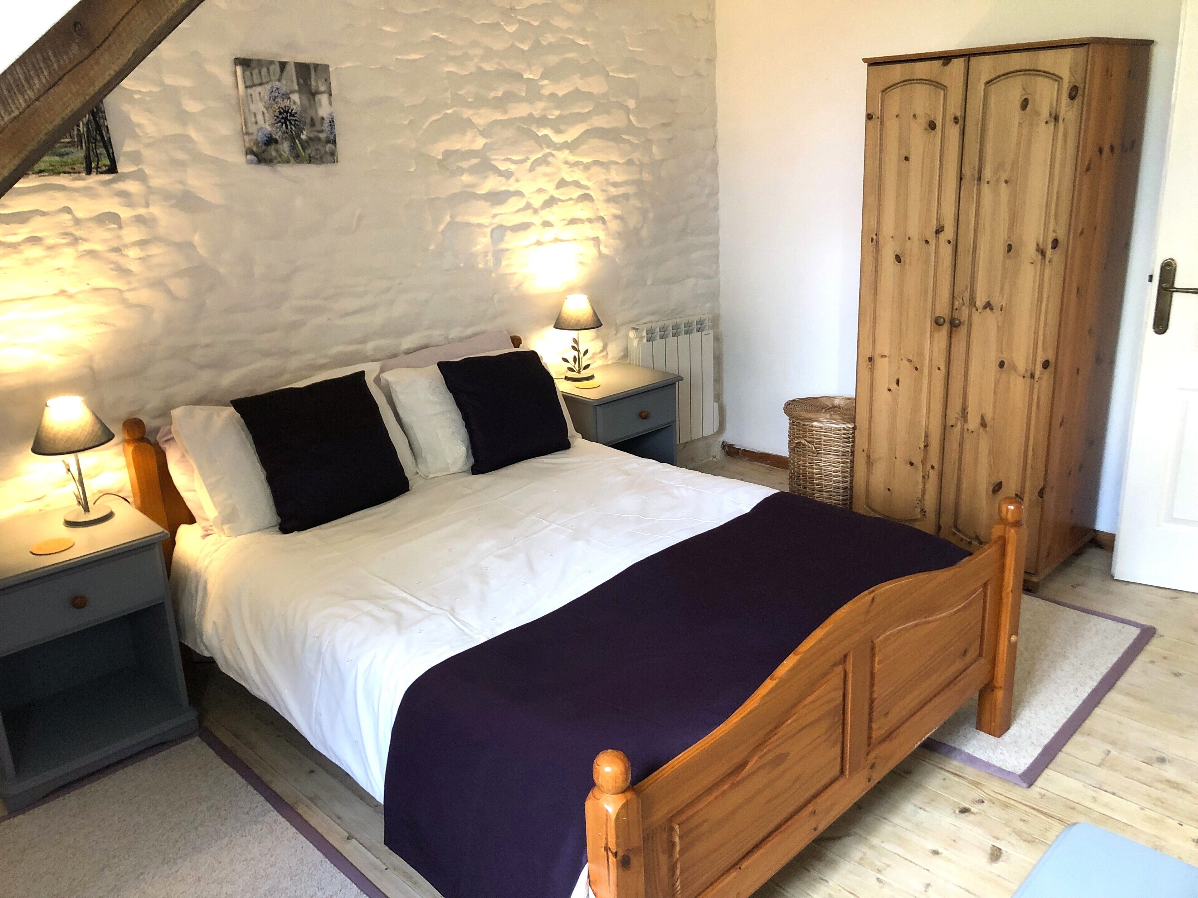 A bedroom with a wooden bed, white walls, and a wooden wardrobe.