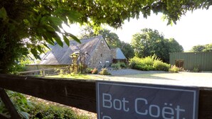 Schild für Bot Coët Cottages, mit einem Steinhaus und einem Holzzaun im Hintergrund.