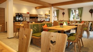 A cozy restaurant with wooden furniture, green cushioned benches, and a bar area with a coffee machine. - Apartments Schmiedgut (Haus)