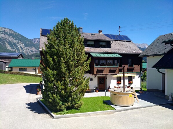 A two-story chalet with a sloped roof, wooden balconies, and a large coniferous tree in the front yard.