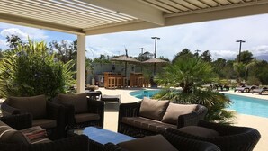 A covered outdoor area with wicker furniture, a pool, and umbrellas.