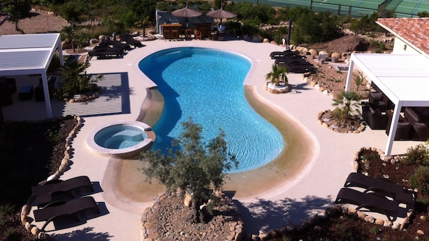 A swimming pool with lounge chairs and umbrellas, surrounded by a landscaped area with rocks and plants.