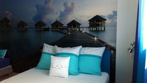 A bedroom with a bed, pillows, and a mural of overwater bungalows.
