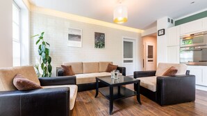 A modern living room with a sofa set, a coffee table, and a dining area with a kitchen in the background. - Victus Apartamenty - Walor 2 (Sopot)