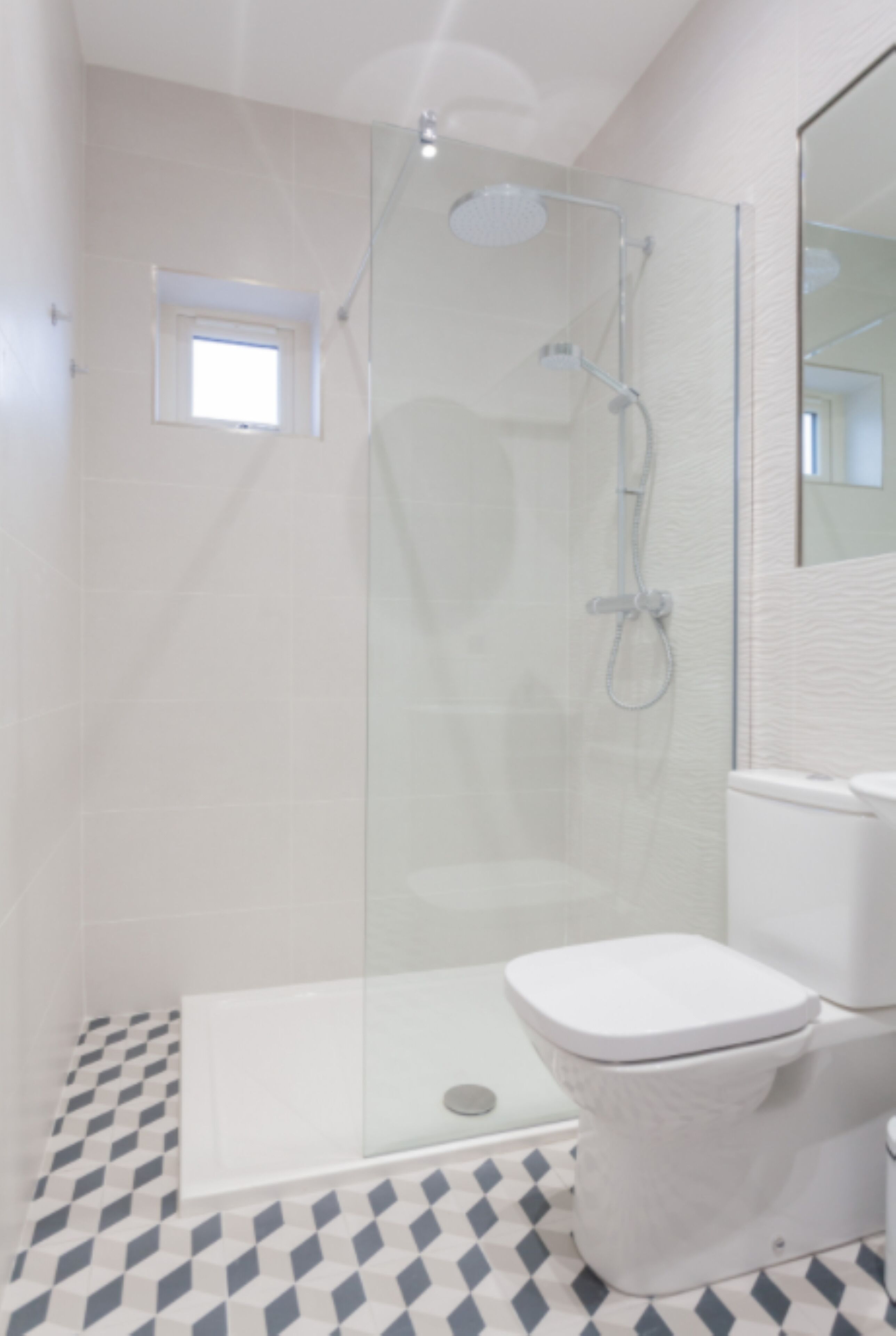 Un baño moderno con ducha de vidrio, inodoro blanco y piso estampado.