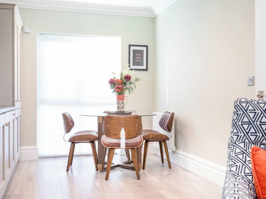 Un comedor con una mesa y cuatro sillas, un florero con flores, un cuadro en la pared y un sofá estampado.
