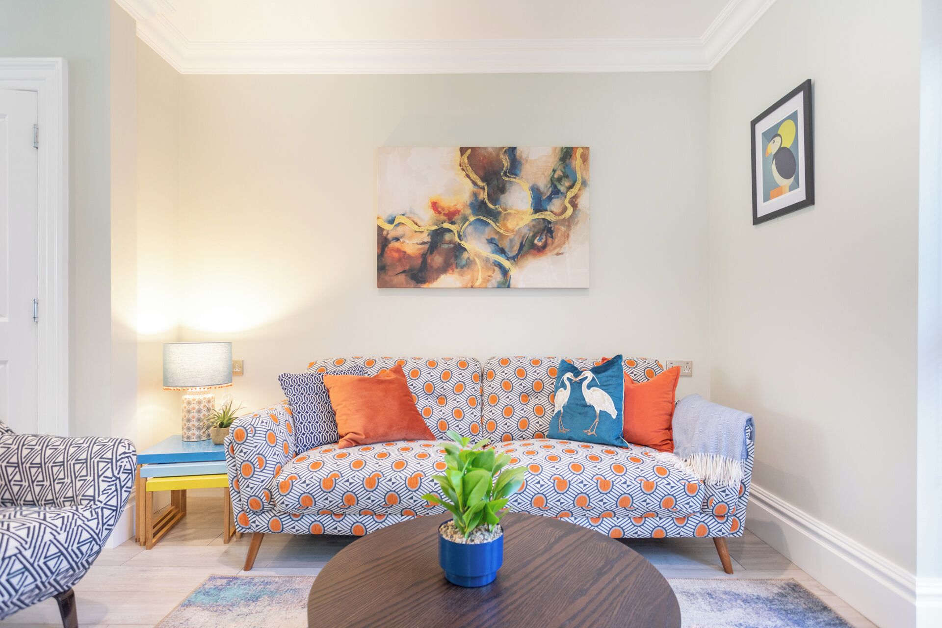 Una sala de estar con un sofá estampado, una mesa de centro con una planta y un cuadro en la pared.