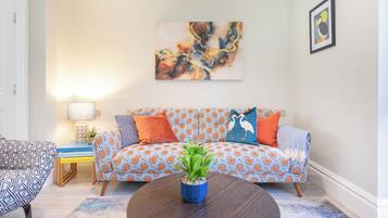 Una sala de estar con un sofá estampado, una mesa de centro con una planta y un cuadro en la pared.