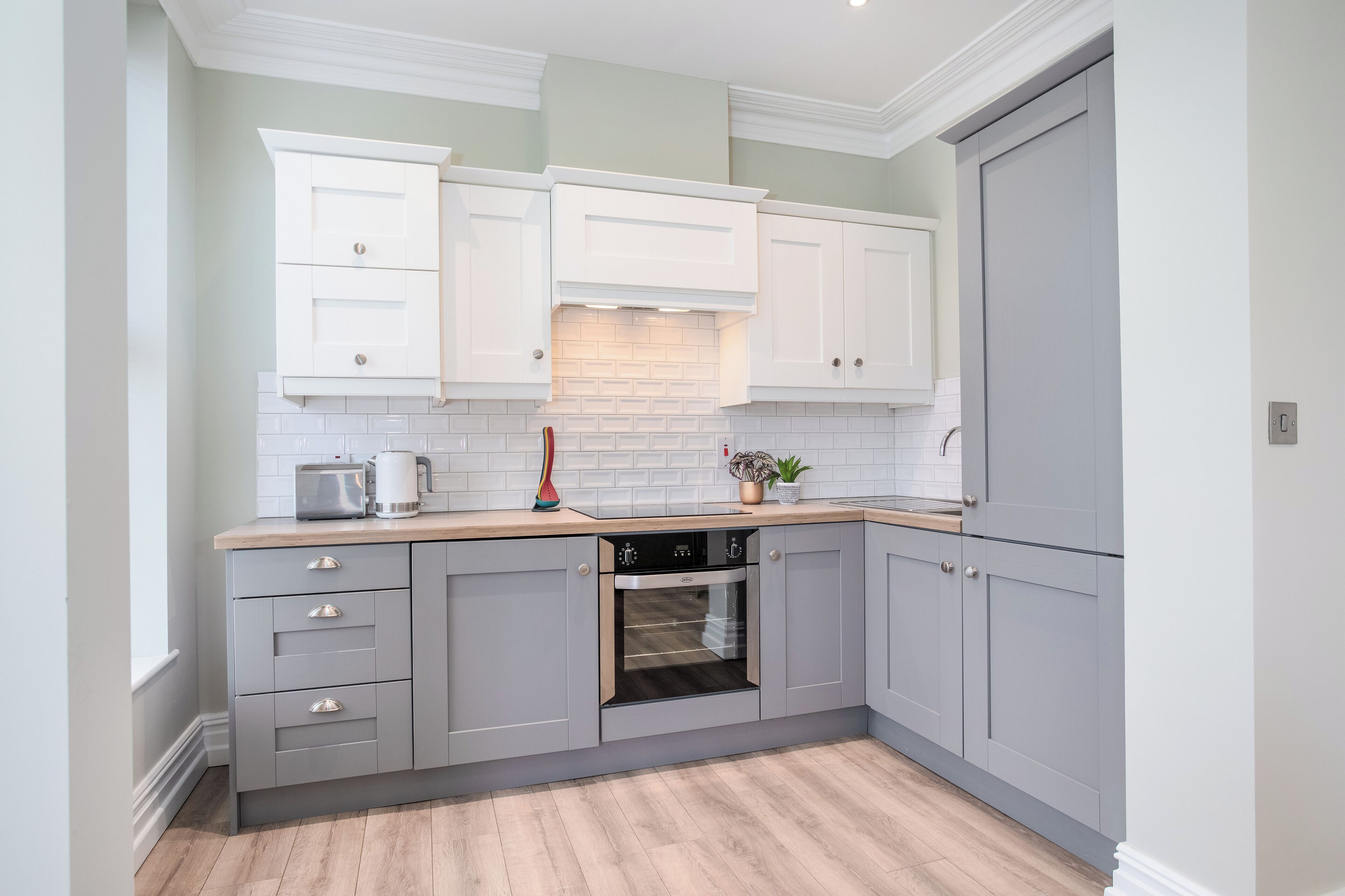 A modern kitchen with grey cabinets, a built-in oven, and a wooden countertop.