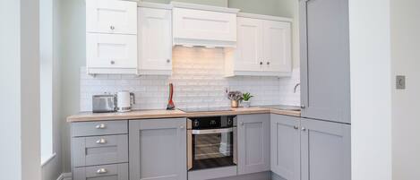 A modern kitchen with grey cabinets, a built-in oven, and a wooden countertop.
