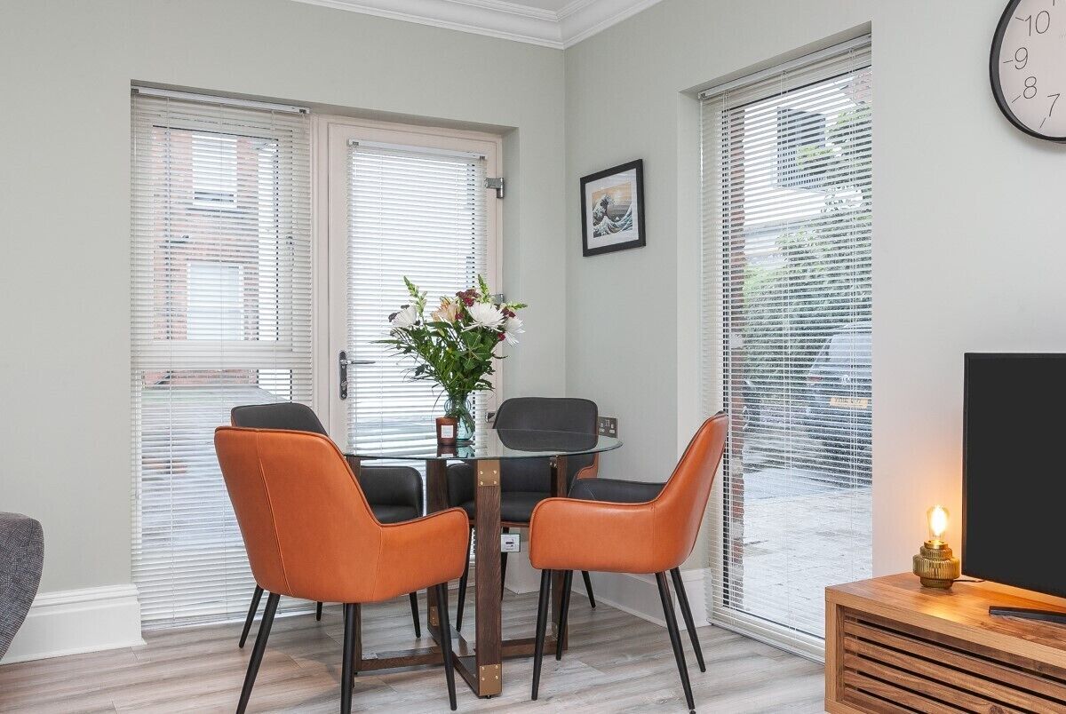 A dining area with a round table, four chairs, and a potted plant.