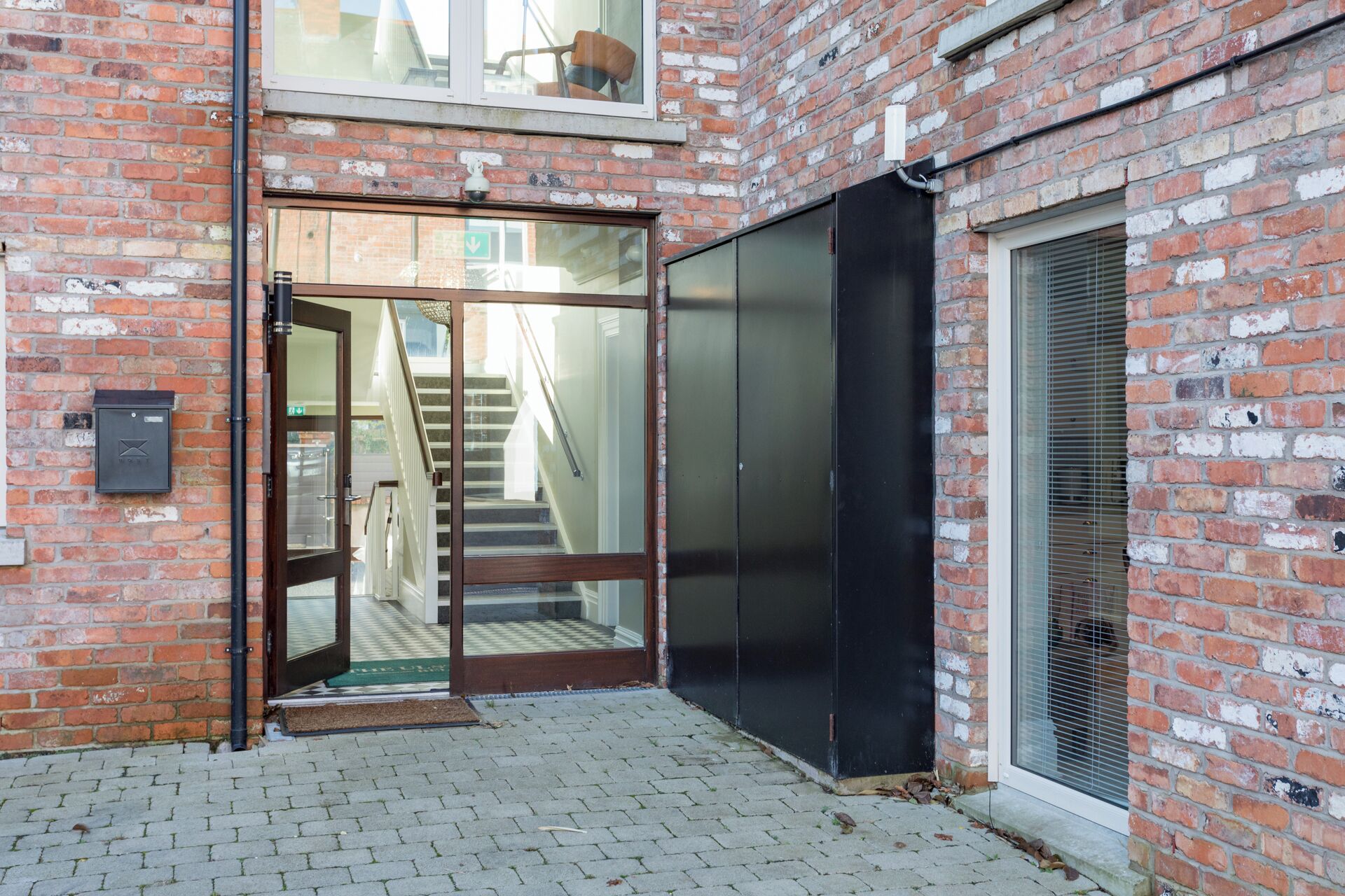 A brick building with a glass door entrance, a staircase, and a black sliding door.
