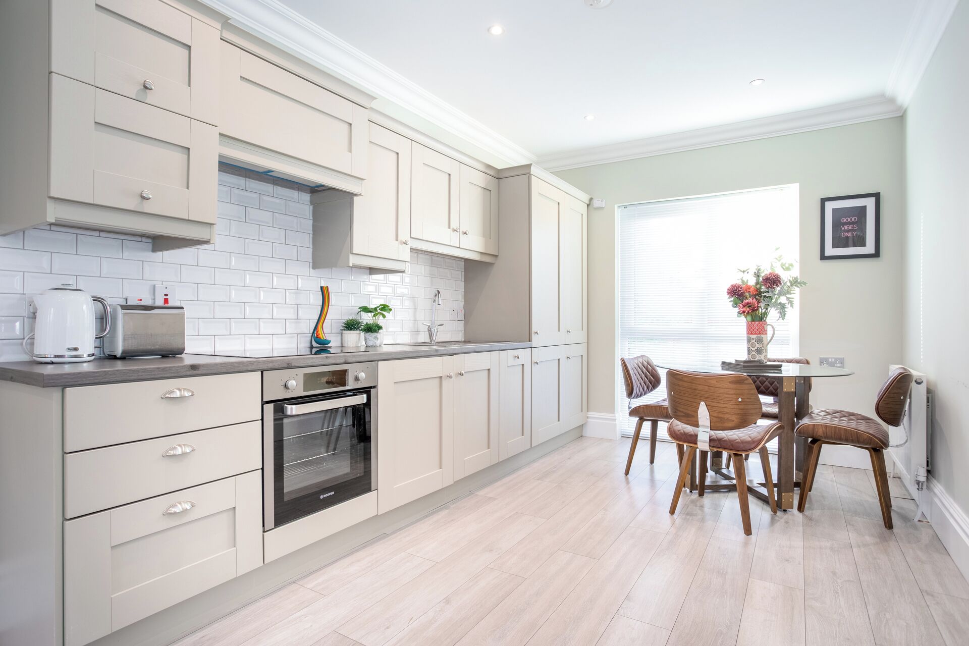 A modern kitchen with white cabinets, a built-in oven, and a dining area with a table and chairs.