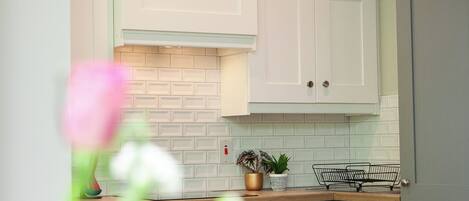 A kitchen with white cabinets, a brick backsplash, and a wooden countertop.