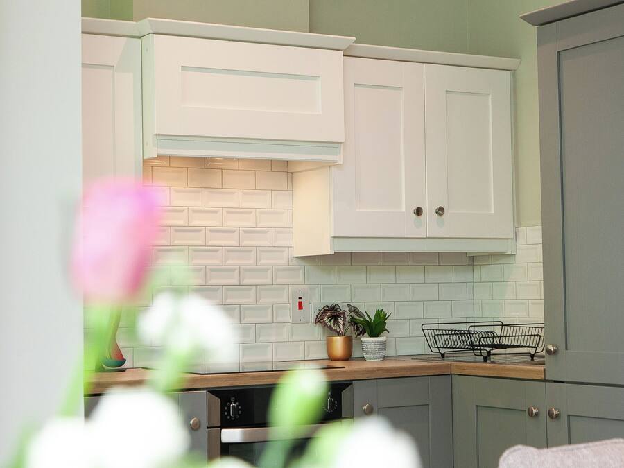 A kitchen with white cabinets, a brick backsplash, and a wooden countertop.