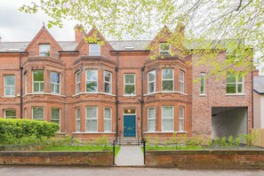 A red brick Victorian-style building with bay windows, a central entrance, and a small garden area.