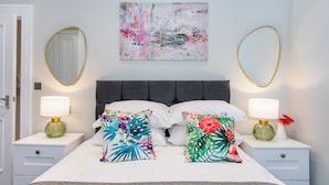 A neatly made bed with floral pillows, two bedside lamps, and a large abstract painting on the wall. - The Ulsterville Residences (Belfast)