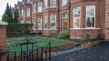A row of red brick houses with bay windows and a well-maintained lawn.