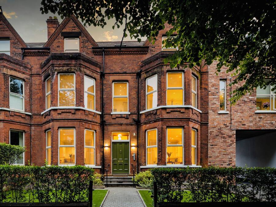 A Victorian-style brick house with bay windows, a green door, and a well-maintained front garden.