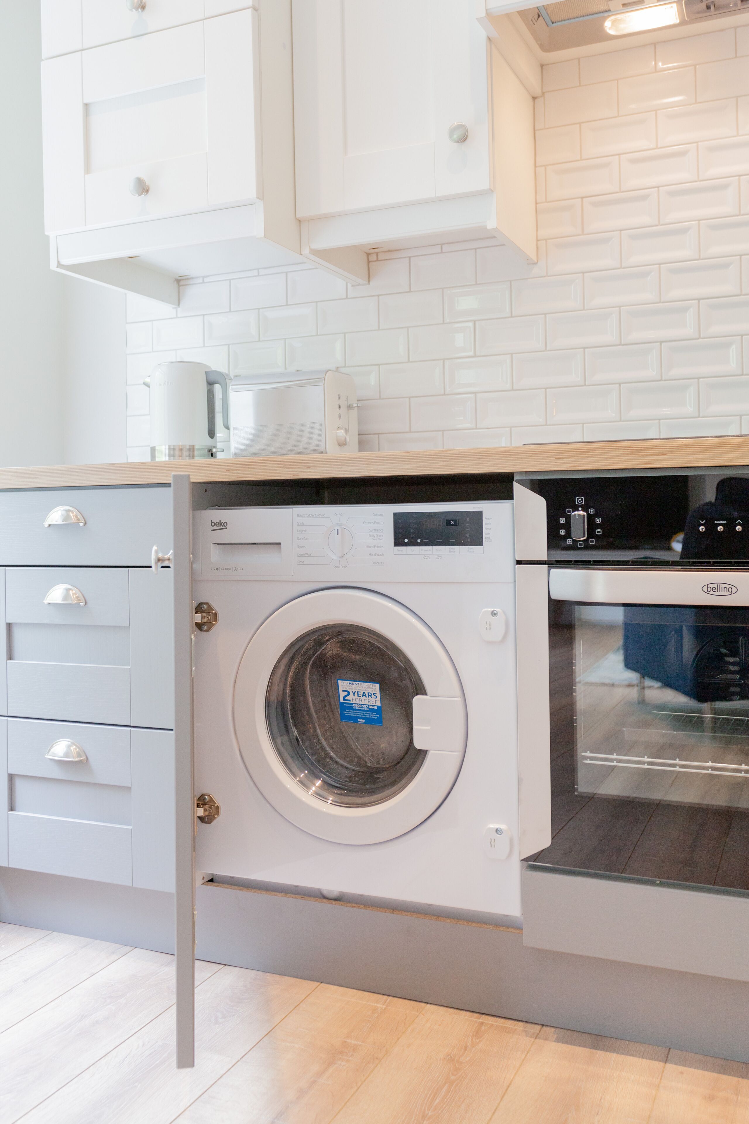 A compact kitchen with a front-loading washing machine, a built-in oven, and white cabinetry.