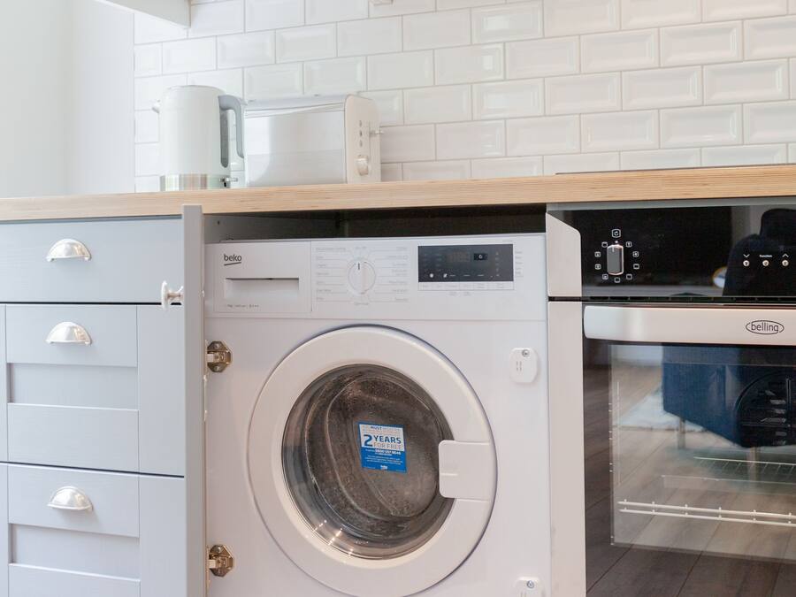 A compact kitchen with a front-loading washing machine, a built-in oven, and white cabinetry.
