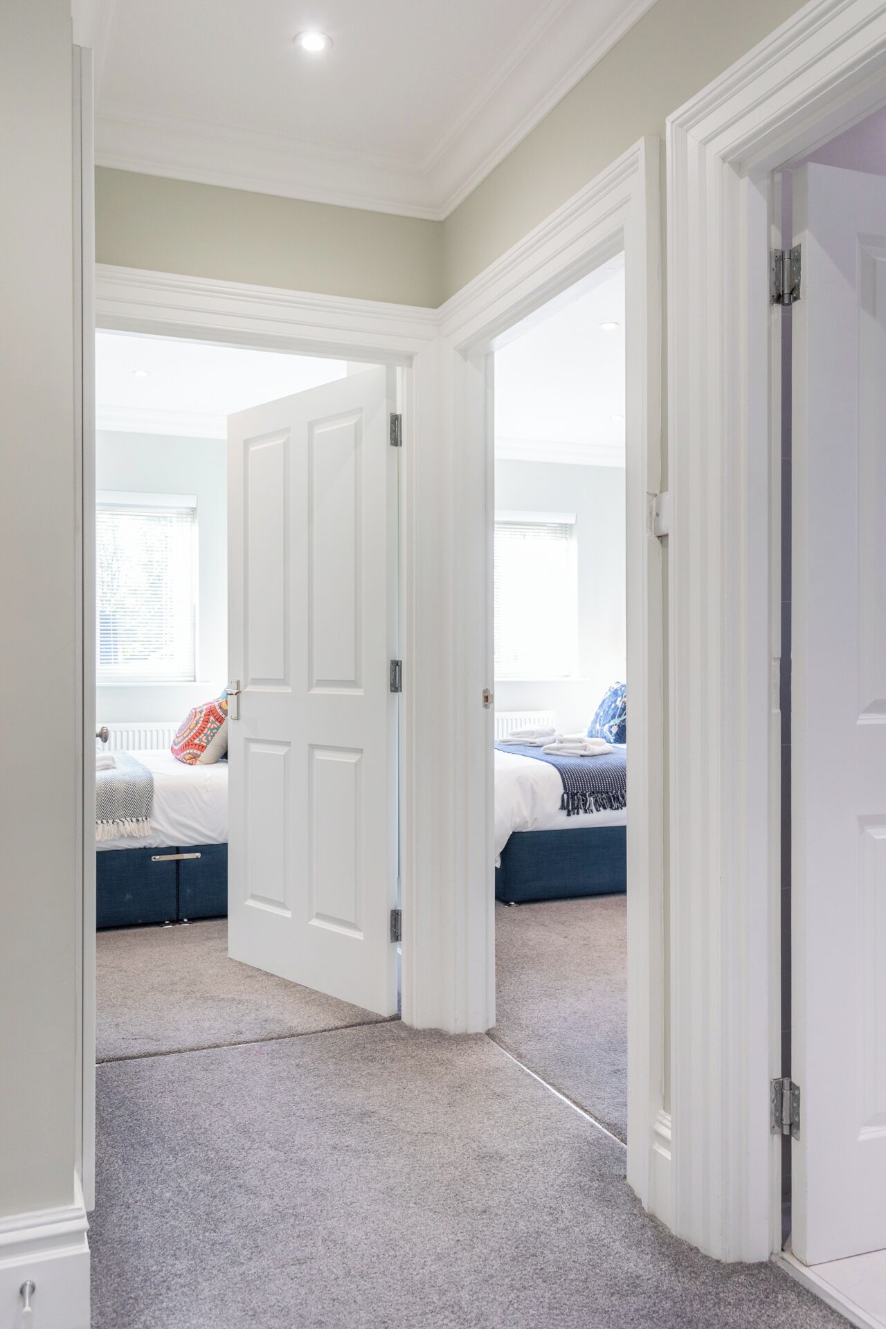 A room with a large white door, carpeted floor, and a bed with a blue headboard.