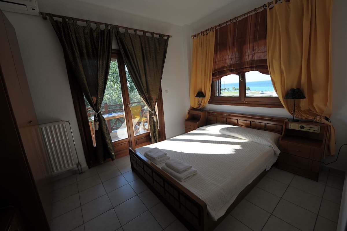 Ein Schlafzimmer mit Bett, Vorhängen, einem Fenster mit Aussicht, einem Heizkörper und einer Lampe auf einem Nachttisch.