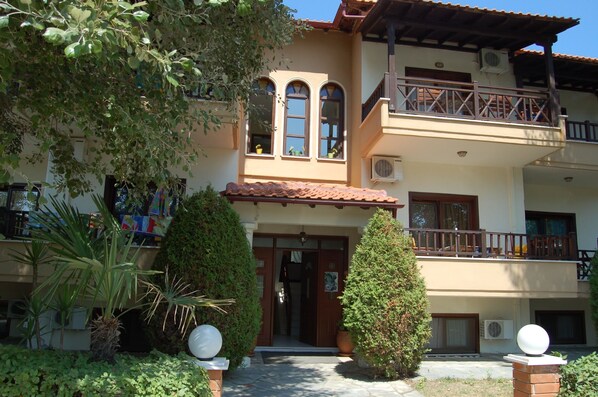 A two-story building with a balcony, a door, and a small garden area with plants.