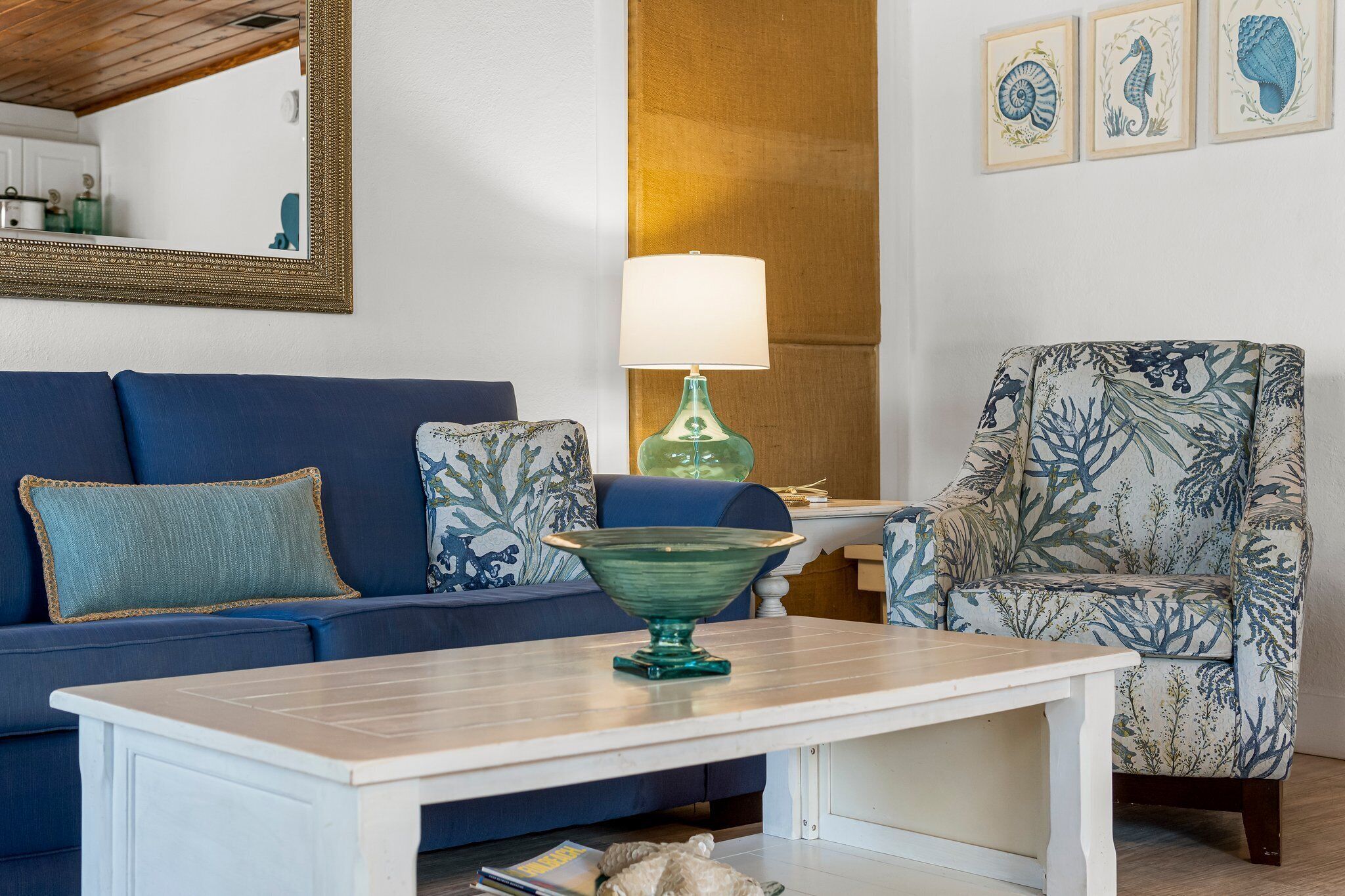 Een woonkamer met een blauwe bank, een groene tafellamp en een fauteuil met een patroon.