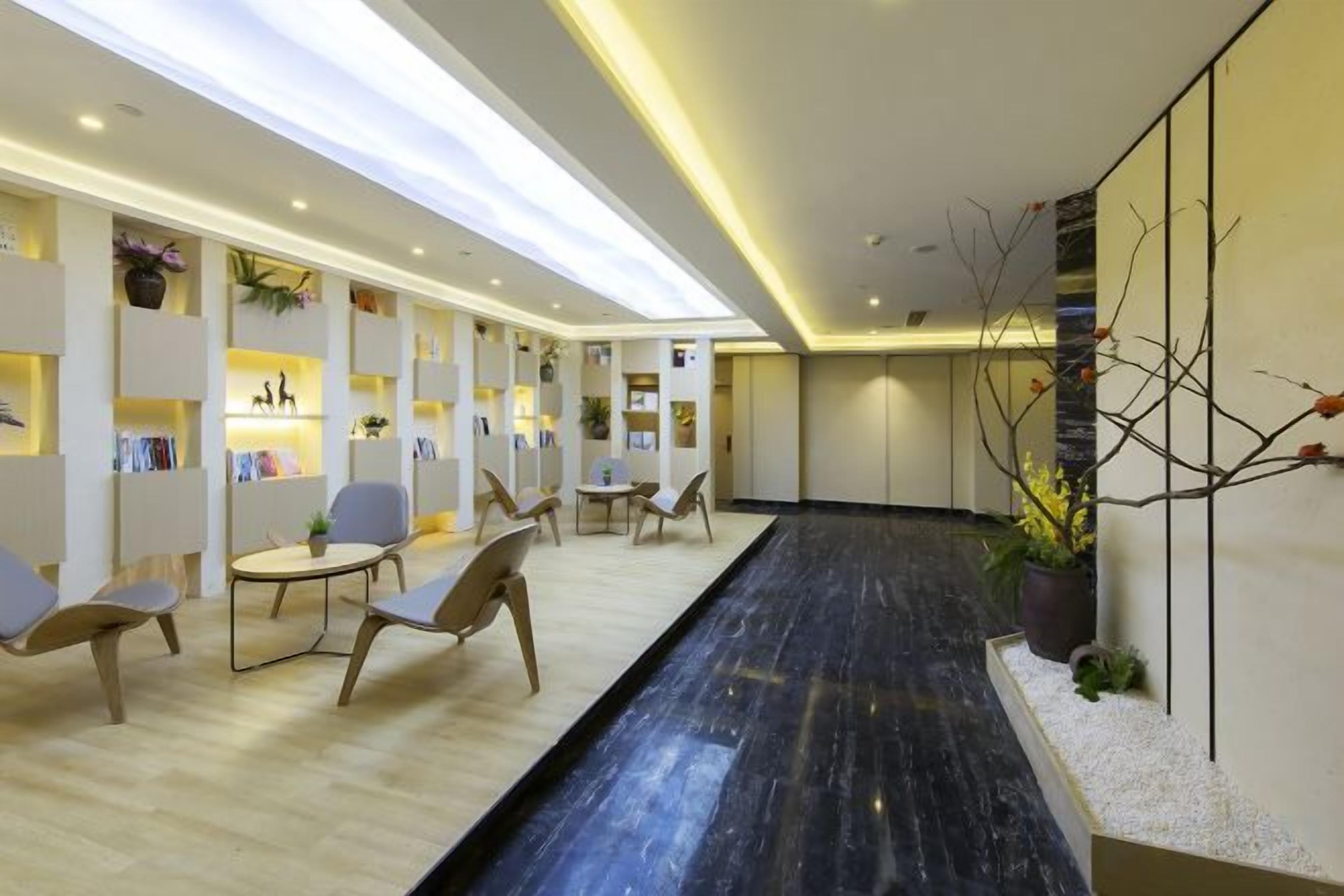 A modern hotel lobby with a long reception desk, seating area, and decorative plants.