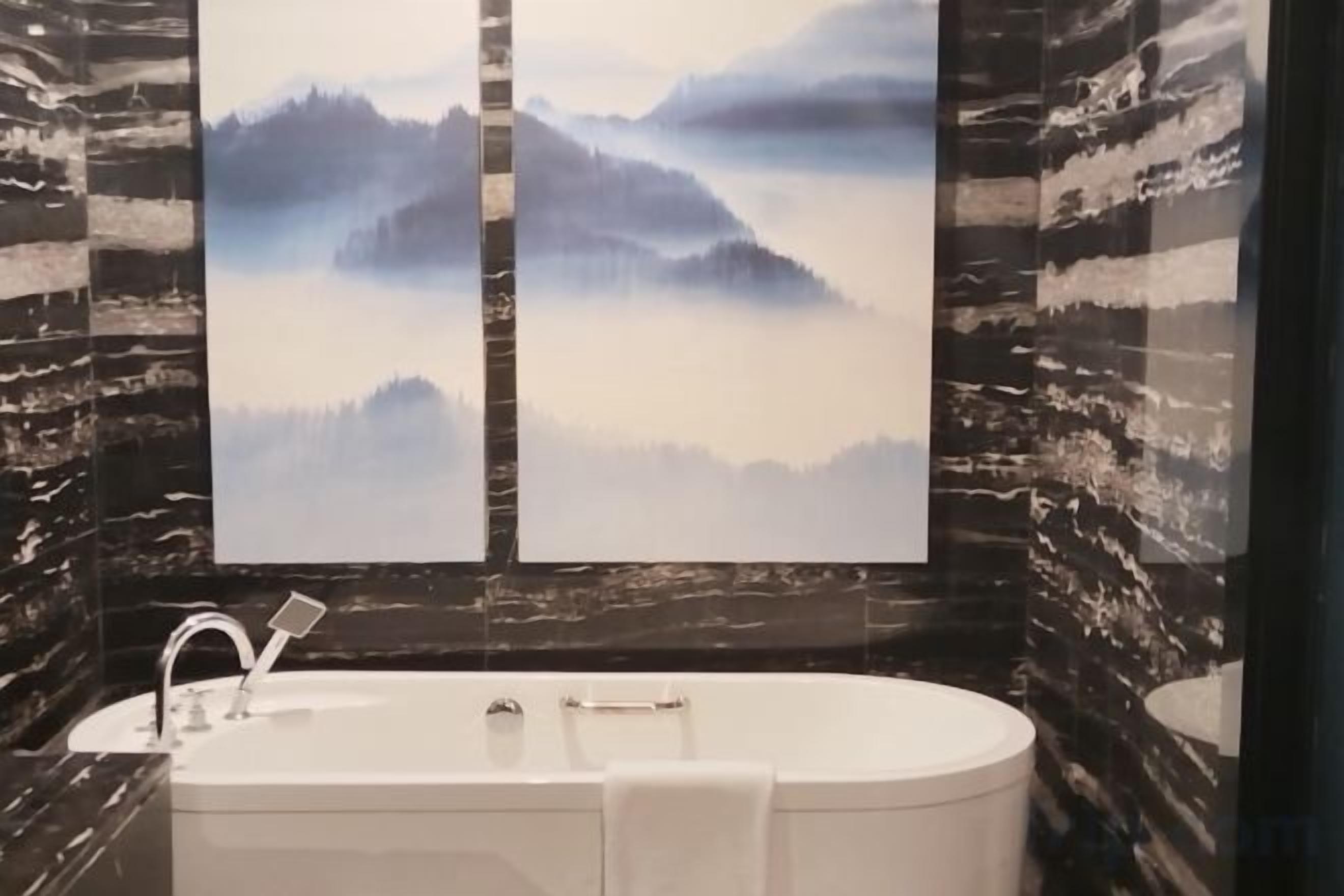 Un baño con una bañera independiente, un lavabo de pared y dos grandes cuadros de paisajes.