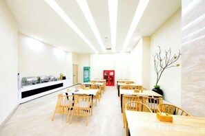 A bright, modern dining area with wooden tables and chairs, a buffet counter, and a red vending machine. - Putian Hotel (Xiamen Mingfa Plaza) (Xiamen)