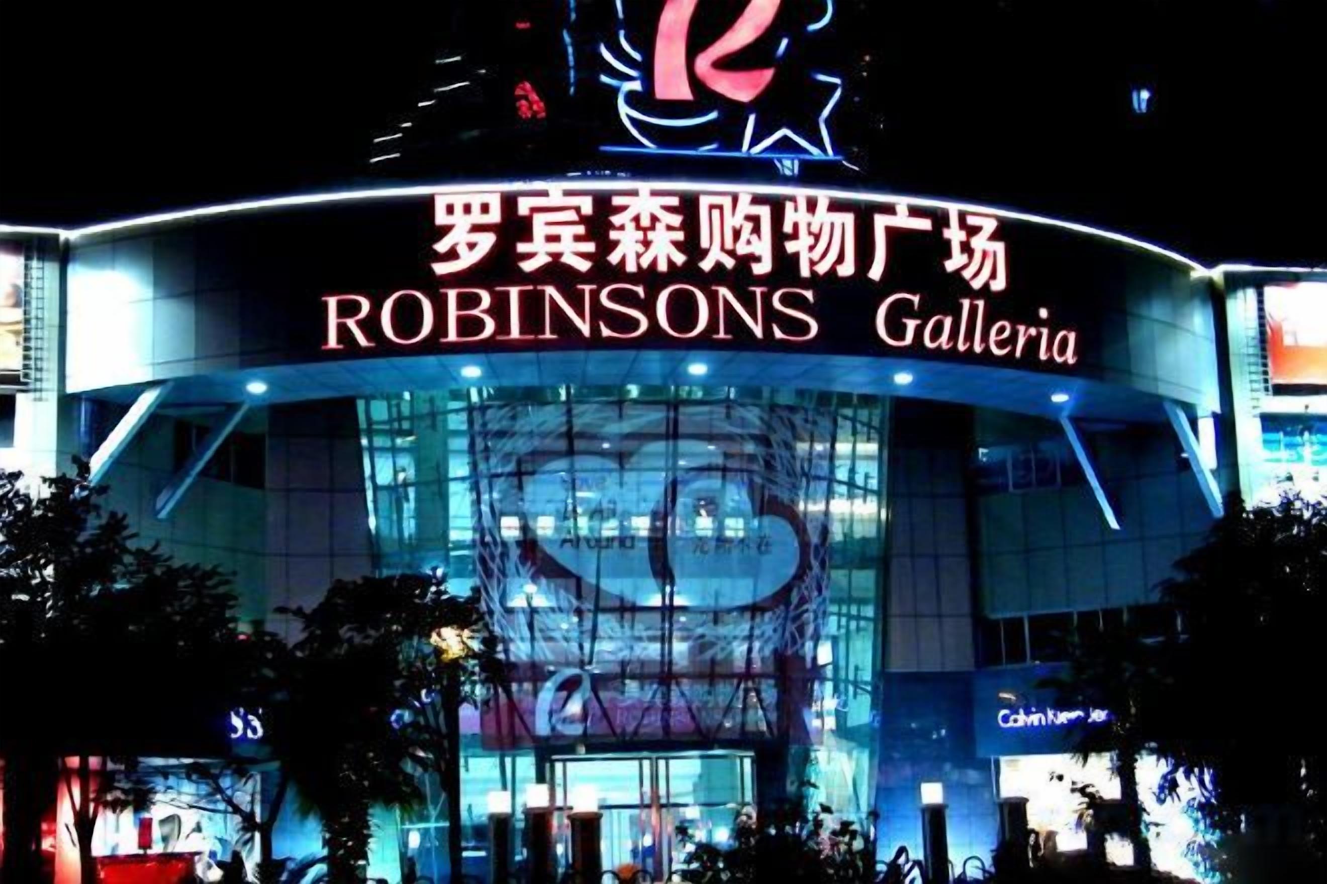 Un edificio moderno con un letrero grande que dice 'ROBINSONS Galleria' de noche.