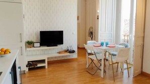 A modern living room with a flat-screen TV, a dining table with chairs, and a small shelf with a plant and a sign. - Cozy apartment with Beautiful Views (Sevilla)