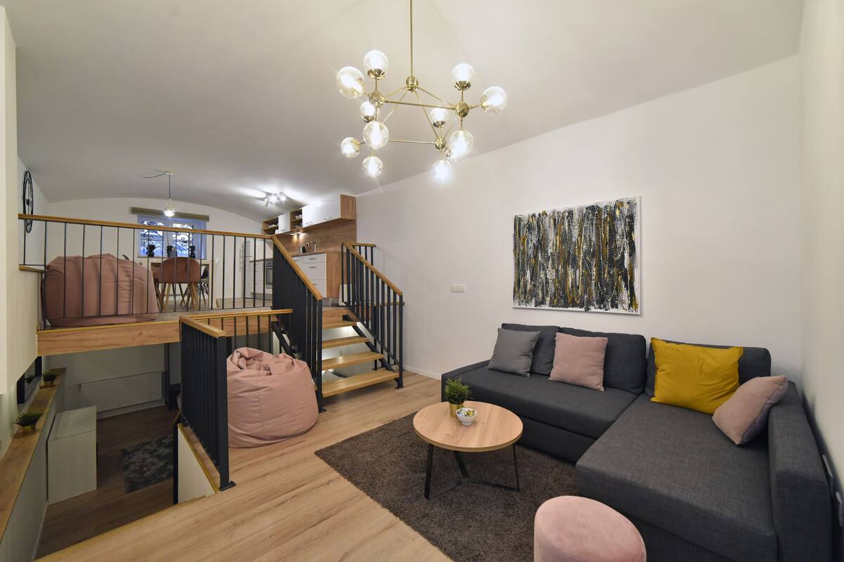 Ein modernes Wohnzimmer mit Treppe, einem grauen Sofa, einem Holztisch und einer Pendelleuchte.