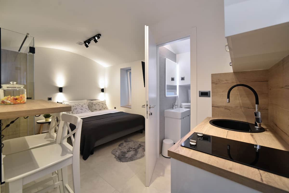 Ein modernes Schlafzimmer mit Bett, Nachttisch und einem kleinen Schreibtisch mit Stuhl. Es gibt ein Badezimmer mit Waschbecken und Spiegel.