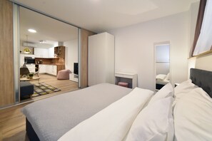 Une chambre d’hôtel moderne dotée d’un grand lit, d’une table de chevet, d’un miroir et offrant une vue sur la cuisine et l’espace de vie grâce à une porte coulissante.