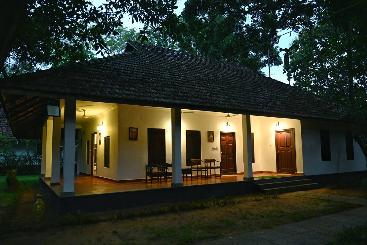 A traditional building with a tiled roof, a porch with chairs, and a door.