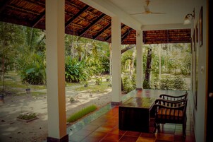 Un espacio al aire libre cubierto con una mesa y sillas, rodeado de abundante vegetación y vistas al exterior.