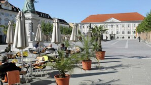 Ein Straßencafé mit Tischen, Stühlen und Sonnenschirmen, umgeben von Blumentöpfen.