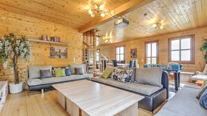 Ein gemütliches Blockhaus-Interieur mit Holzboden, einer Sofagarnitur, einem Couchtisch, einem Bücherregal und einer Treppe.