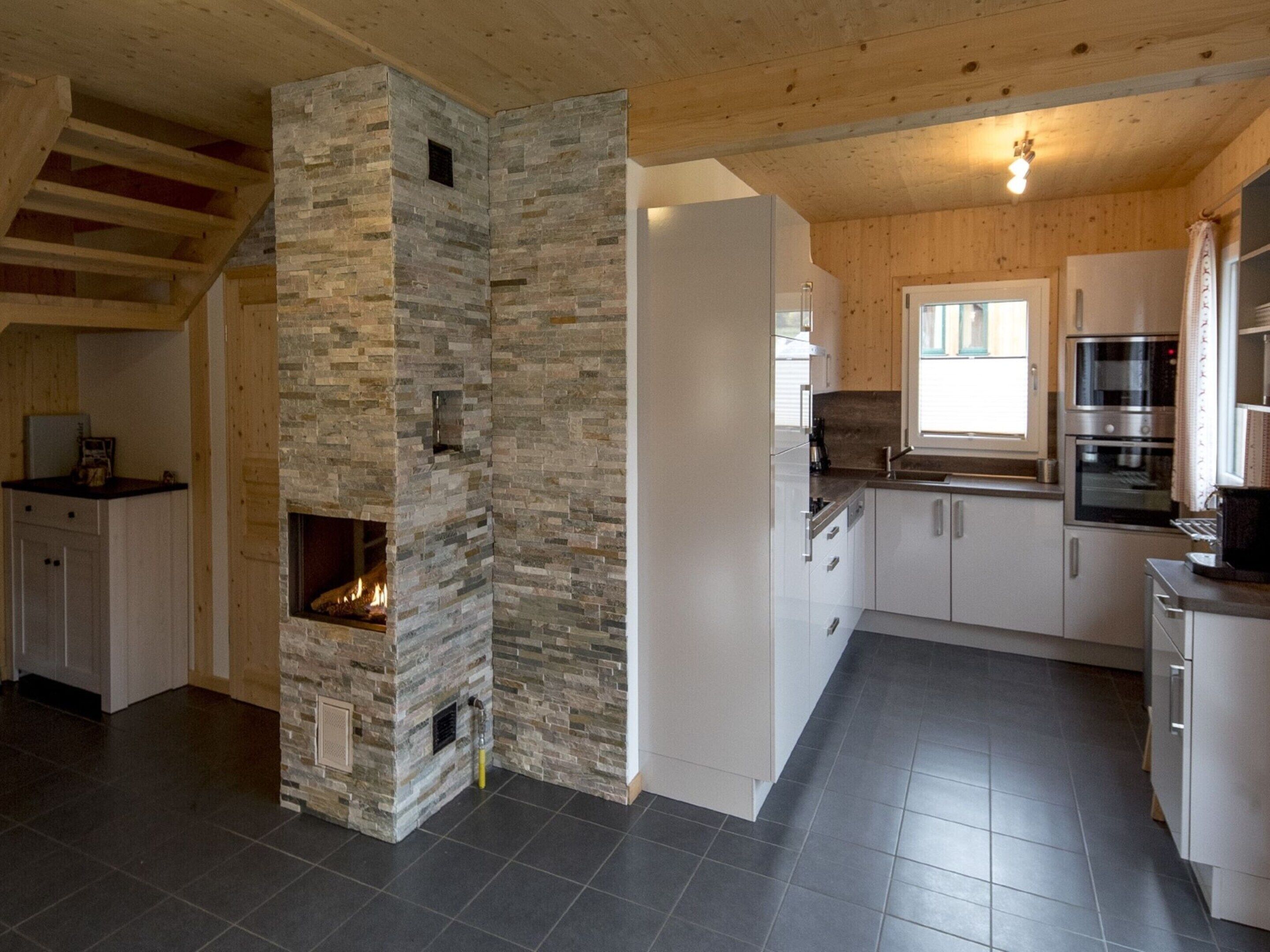 Eine moderne Küche mit Kamin aus Stein, weißen Schränken und einem eingebauten Ofen.