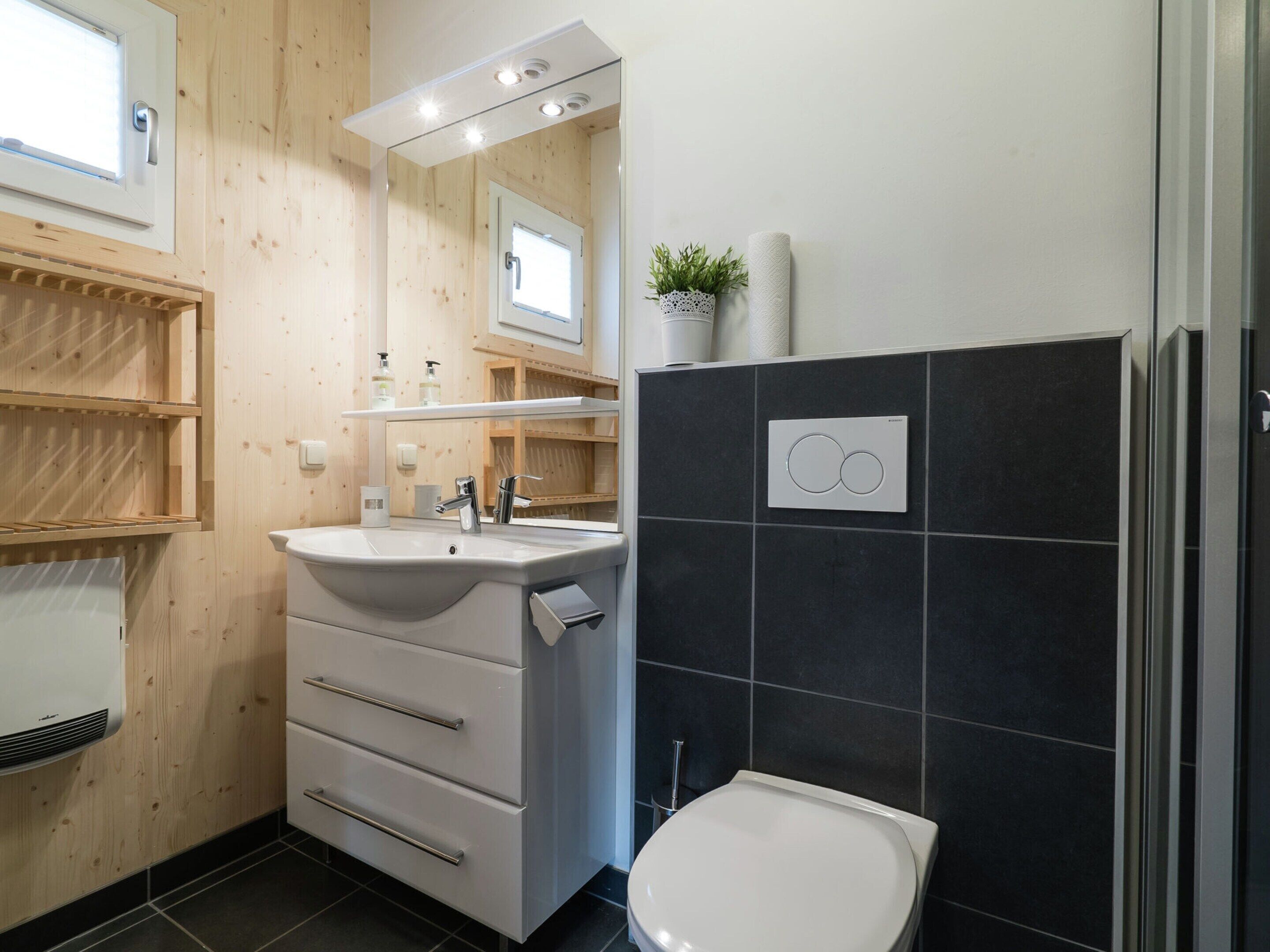 A bathroom with a wooden vanity, a white sink, a mirror, a toilet, and a wall-mounted heater.