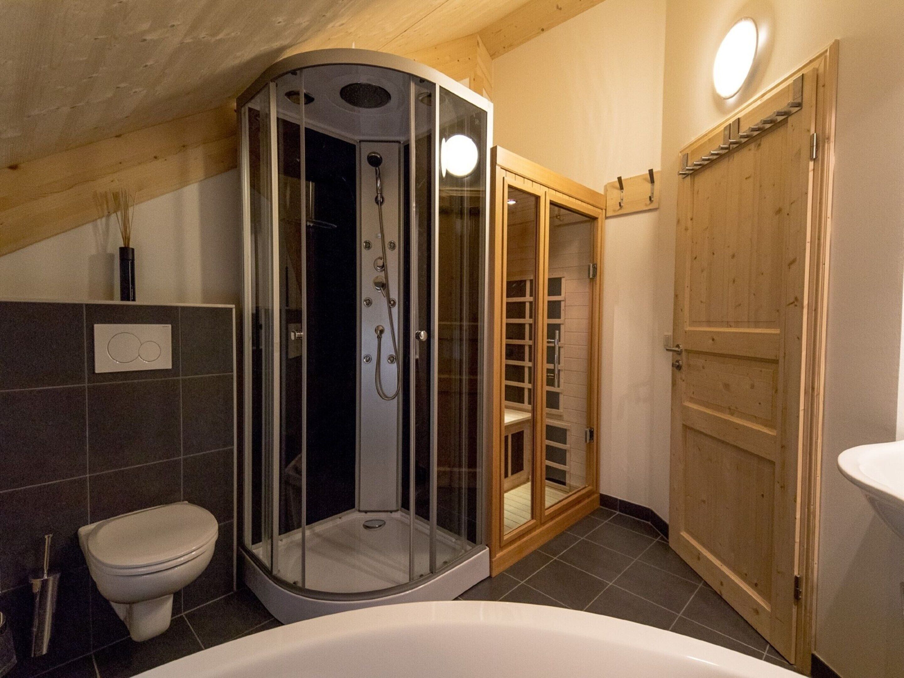 A bathroom with a glass-enclosed shower, a toilet, and a wooden door.