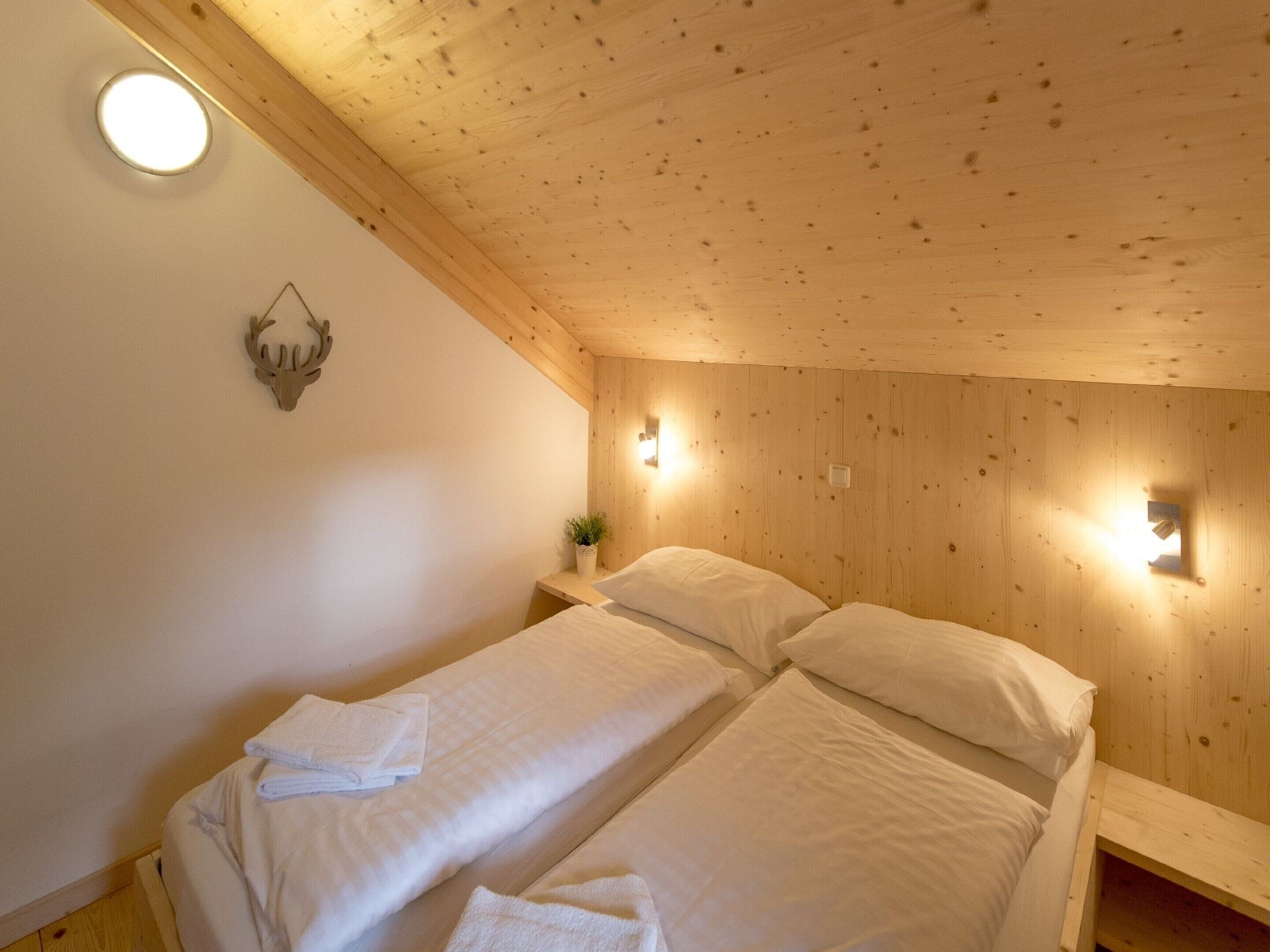 A wooden cabin room with two beds, a wall-mounted light, and a small plant on a nightstand.