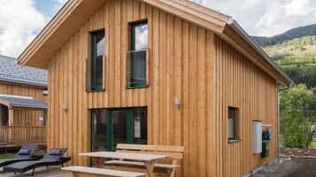 A wooden cabin with a deck, two windows, and a small outdoor seating area.