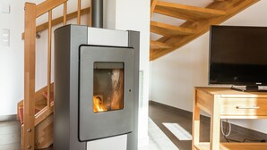 A modern living room with a wood-burning stove, a wooden staircase, and a television on a wooden table. - Chalet in Carinthia With Sauna Near Ski Slopes (Frantschach-Sankt Gertraud)