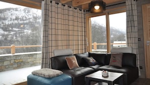A cozy room with a sofa, a small table, and a view of snowy mountains through large windows. - Cosy Valloire Family Chalet (Valloire)